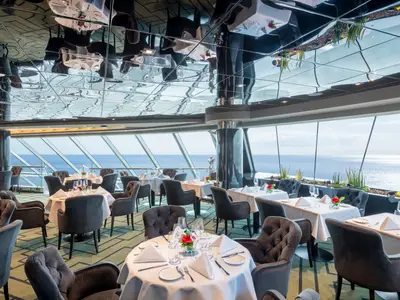 Elegantes Restaurant an Bord der MSC Virtuosa mit vielen gedeckten Tischen. Grosse Fenster bieten einen weiten Blick auf das offene Meer.