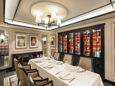 Ein langer, gedeckter Esstisch in einem eleganten Spezialitätenrestaurant Indochine an Bord der MSC Virtuosa. Der Raum ist mit Kunstwerken und beleuchteten Vitrinen dekoriert.