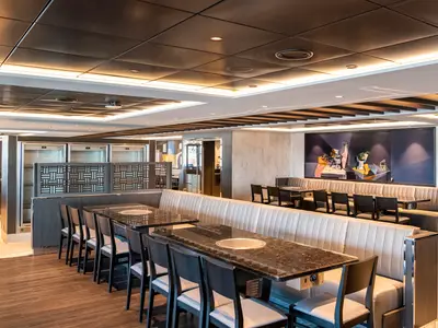 Modernes Restaurant Sea Pavilion an Bord der MSC Virtuosa. Granittische mit Grillplatten, helle Sitzbänke, grosses Wandgemälde und moderne Beleuchtung prägen den Raum.