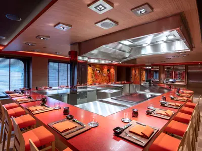 Spezialitätenrestaurant Kaito Teppanyaki auf der MSC Virtuosa. Rote Theken um Kochstationen, orangefarbene Stühle und japanische Wandkunst. Modernes Design.