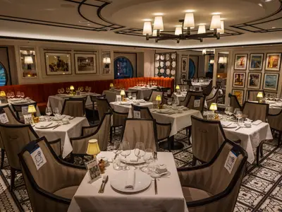 Indochine Restaurant an Bord der MSC Virtuosa, mit gedeckten Tischen, warmer Beleuchtung, gemustertem Boden und Kunstwerken an den Wänden.
