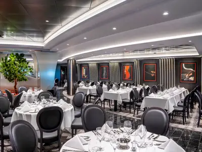Ein stilvolles Restaurant an Bord der MSC Virtuosa, mit vielen weiß gedeckten Tischen, dunklen Stühlen und Kunstwerken mit Musikinstrumenten an den Wänden. Grüne Pflanzen schmücken den Raum.