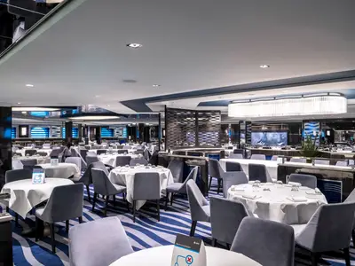 Das moderne Restaurant 'Blue Danube' an Bord der MSC Virtuosa. Zahlreiche Tische, graue Stühle, blaue Wellenmuster und eine lange Deckenleuchte schaffen elegantes Ambiente.