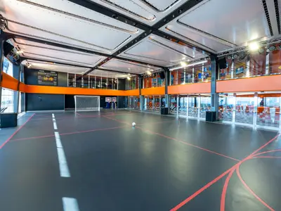 Multifunktionaler Sportplatz an Bord der MSC Virtuosa. Dunkler Boden, rote Linien, Fussballtor, Basketballkörbe, Ball, Anzeigetafel und grosse Fenster sind sichtbar.