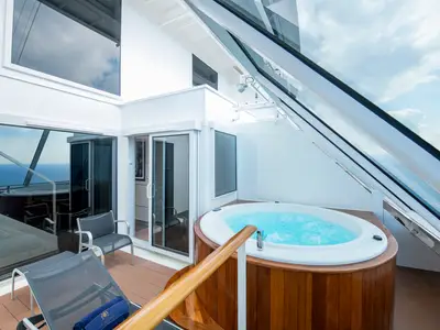 Terrasse einer Luxussuite auf der MSC Virtuosa. Ein sprudelnder Whirlpool aus Holz, Liegestühle und Glasfronten zum Meer. Im Hintergrund sind blauer Ozean und Himmel zu sehen.