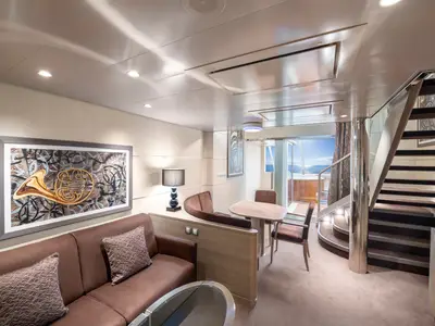Luxuriöse Duplex Suite an Bord der MSC Virtuosa. Wohnbereich mit Sofa, Esstisch, Treppe und Balkon mit Whirlpool und Meerblick. Elegante Einrichtung.