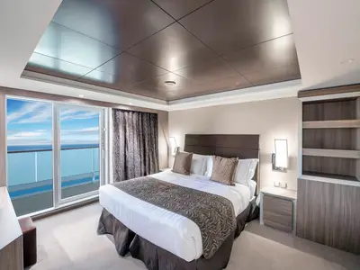 Moderne Suite an Bord der MSC Virtuosa. Die Kabine ist mit einem großen Doppelbett, Nachttischen und Regalen ausgestattet. Durch die Balkontür bietet sich ein weiter Blick auf das Meer.