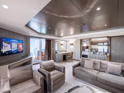 Geräumige Royal Suite an Bord der MSC Virtuosa mit modernem Wohnbereich, Sofas, TV und Schreibtisch. Ein Balkon ist durch die Glastür sichtbar, dahinter ein Doppelbett.
