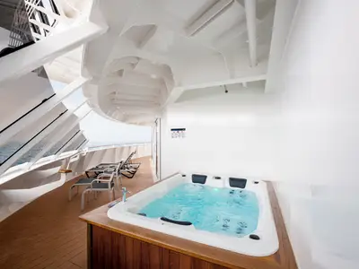 Blick auf eine luxuriöse private Suite-Terrasse an Bord der MSC Virtuosa mit sprudelndem Whirlpool, Holzdeck und weitem Meerblick. Mehrere Liegestühle laden zum Entspannen ein.