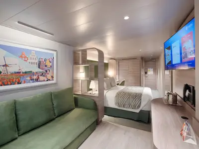Geräumige, modern eingerichtete Außenkabine an Bord der MSC World America. Sichtbar sind ein großes Sofa, ein Doppelbett, ein Schreibtisch und ein Flachbildfernseher. An der Wand hängt ein großes Kunstwerk von Amsterdam mit Windmühlen und Tulpenfeldern.