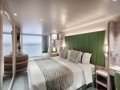 Eine helle, moderne Aussenkabine der MSC World America mit Doppelbett, grünem Kopfteil und Sofa. Eine grosse Fensterfront bietet direkten Blick auf das Meer. Möbel in hellem Holz.