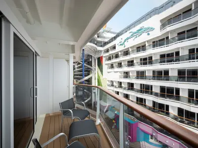 Blick von einer Balkonkabine auf der MSC World America. Man sieht die Promenade, eine hohe Wasserrutsche und viele weitere Balkone. Der eigene Balkon ist mit zwei Stühlen ausgestattet.