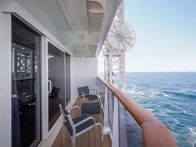 Eine helle Grand Suite Aurea Balkonkabine an Bord der MSC World America mit drei Outdoor-Stühlen und Blick auf das weite, blaue Meer und den Himmel.