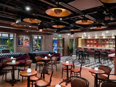 Die elegante The Loft Comedy & Live Music Bar an Bord der MSC World America. Der Raum zeigt bequeme Sitzgruppen, eine rote Bar, stylische Deckenbeleuchtung und Fenster.