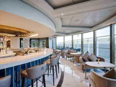 Blick in die Fizz Champagne Bar der MSC World America mit gebogener Theke, Barhockern, Lounge-Sitzbereichen und großen Fenstern zum Meer und Außendeck.