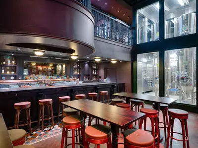 Die Bar 'Masters of the Sea' an Bord der MSC World America zeigt eine dunkle Holztheke und rote Hocker. Im Hintergrund sind glänzende Bierbrau-Tanks durch Glas sichtbar. Eine elegante, warme Atmosphäre.