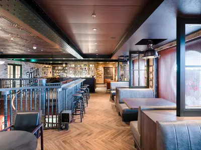Die Bar 'The Gin Project' an Bord der MSC World America. Man sieht eine lange Bar mit Stühlen, Sitzbänken und Tischen in einem modern-rustikalen Ambiente mit Backsteinwänden und kunstvollen Decken.