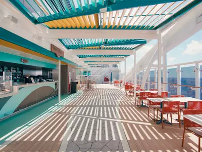 Die Harbour Bar & Bites an Bord der MSC World America. Ein langer Bartresen und ueberdachte Sitzbereiche mit roten Stühlen und Meerblick.
