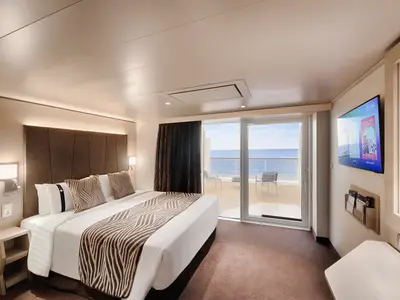 Helle, moderne Balkonkabine an Bord der MSC World America mit Doppelbett, Wand-TV und direktem Zugang zum Balkon mit Meerblick. Die Einrichtung ist in warmen Braun- und Beigetönen gehalten.