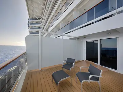Balkon an Bord der MSC World America. Holzterrasse mit zwei Stühlen und Hocker. Blick auf das offene Meer und weitere Schiffsbalkone.