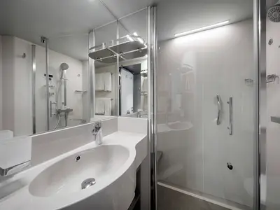 Badezimmer an Bord der MSC World America mit Dusche, Waschtisch und Spiegel. Die Dusche hat Haltegriffe, die Einrichtung ist modern und hell.