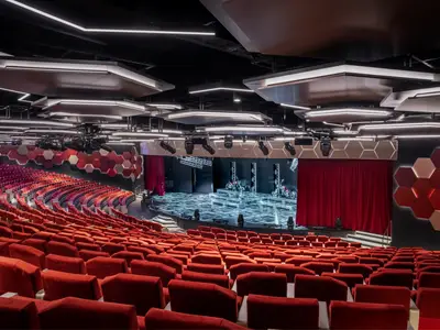 Das World Theatre der MSC World America mit roten Sitzen und beleuchteter Bühne mit Motorrädern. Moderne Architektur, hexagonale Wände, futuristische Deckenleuchten.