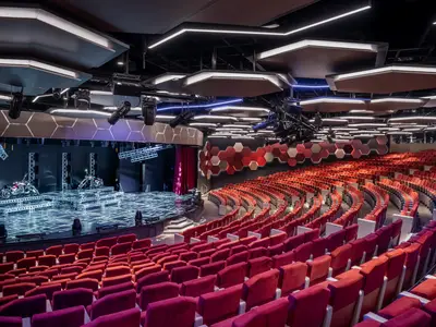 Blick ins futuristische Theater an Bord der MSC World America mit einer großen Bühne, auf der zwei Motorräder stehen. Die roten Sitzreihen sind leer, die Decke ist mit modernen Leuchten ausgestattet.