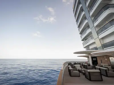 Einladende Outdoor-Lounge auf der MSC World America. Moderne Sitzgruppen unter Schirmen blicken auf das weite, blaue Meer. Die Balkone des Schiffes sind rechts im Bild sichtbar.