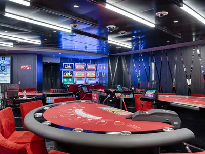 Ein elegantes Casino an Bord der MSC World America mit roten Spieltischen, Roulette und leuchtenden Slotmaschinen.