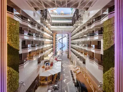 Weitläufige World Promenade der MSC World America. Balkonkabinen, grüne Wände mit Neonlicht. Riesige Spiralrutsche führt zum Meer. Unten Geschäfte und Restaurants.