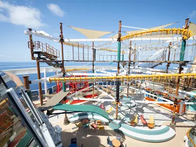 Ausblick auf den riesigen Hochseilgarten auf der MSC World America. Gelbe Kletterparcours und Netze ragen über die Decks. Dahinter das blaue Meer und bunte Sitzgelegenheiten.