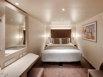 Moderne Innenkabine an Bord der MSC World America. Ein Doppelbett mit Nachttischen ist mittig. Links ein Schminktisch mit Spiegel und Steckdosen. Die Kabine wirkt einladend.
