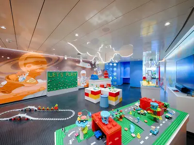 Ein farbenfroher LEGO-Spielraum an Bord der MSC World America. Wände mit Weltraum-Motiven, Spieltische mit LEGO-Steinen, Zugstrecke und Bildschirm.