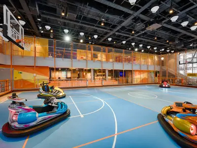 Ein farbenfroher Sportplex an Bord der MSC World America mit Bumper-Cars auf einem Basketballfeld. Zwei Körbe hängen von der Decke. Eine obere Galerie überblickt den Platz.