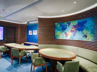 Ein moderner Konferenzraum an Bord der MSC World America mit zwei Tischen, Samtsesseln und einer Rundbank. Eine Weltkarte ziert die gewölbte Holzlattenwand.