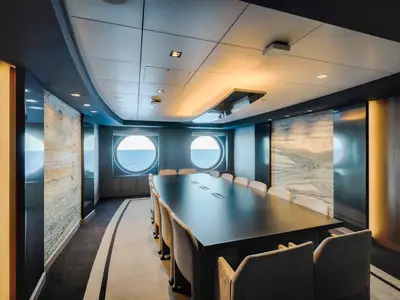 Eleganter Konferenzraum an Bord der MSC World America. Grosser Tisch, Stühle, zwei runde Fenster mit Meerblick. Moderne Einrichtung mit Kunst und Lichtelementen.