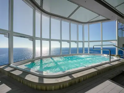Belebter Whirlpool mit blauem Wasser in einem überdachten Poolbereich an Bord der MSC World America. Große Fensterfronten bieten einen weiten Blick auf das sonnige, glitzernde Meer.