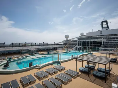 Sonniges Pooldeck der MSC World America: Blaue Pools, Liegestühle, überdachte Lounge-Möbel und eine Seelöwen-Skulptur. Moderne Schiffsarchitektur im Hintergrund.