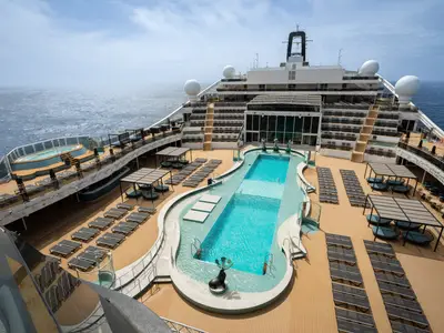 Blick von oben auf das weitläufige Mar Azul Pooldeck der MSC World America mit mehreren Pools, Sonnenliegen und überdachten Lounges. Das offene Meer ist im Hintergrund sichtbar.