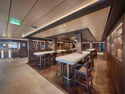 Innenansicht des Il Mercato Buffet an Bord der MSC World America mit langen Bartischen, Holzvertäfelungen, Dekoregalen und einem Service-Tresen im Hintergrund. Der Raum ist hell beleuchtet und modern gestaltet.