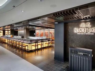 Moderne Kaito Sushi Bar & Teppanyaki an Bord der MSC World America. Eine lange, beleuchtete Theke mit vielen Stühlen. Wandbilder mit Koi-Fischen und eine markante Deckenstruktur.