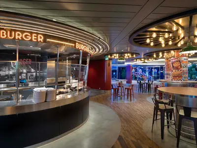 Ein modernes Burger- und Pizza-Restaurant an Bord der MSC World America mit leuchtender Neon-Beschilderung, Essensausgabe und Sitzbereichen.
