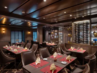 Elegantes Spezialitätenrestaurant an Bord der MSC World America. Festlich gedeckte Tische, braune Lederstühle und ein imposantes Weinregal prägen das Bild. Warme Beleuchtung schafft eine exklusive Atmosphäre.