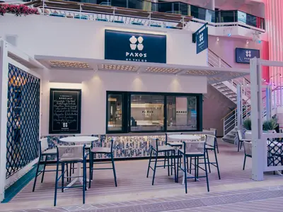 Das Restaurant "Paxos On The Go" an Bord der MSC World America. Modern mit Tresen, hellen Tischen, blauen Stühlen. Im Hintergrund: Treppen und pinke Lichtinstallationen.