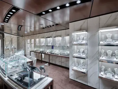 Innenansicht einer luxuriösen Fine Jewellery Boutique an Bord der MSC World America. Zahlreiche Glasvitrinen und Wandregale präsentieren elegant arrangierten Schmuck wie Halsketten, Ringe und Armbänder auf grauen Ständern und Schalen. Die Wände sind mit hellem Marmor verkleidet, und die Decke ist spiegelnd mit integrierten Leuchten versehen. Der Boden ist mit braunem Teppich ausgelegt.