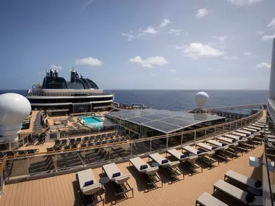 Das weitläufige Sonnendeck der MSC World America unter blauem Himmel, mit vielen Liegestühlen, einem Pool und Blick auf das weite, blaue Meer. Ein idealer Ort zum Entspannen.