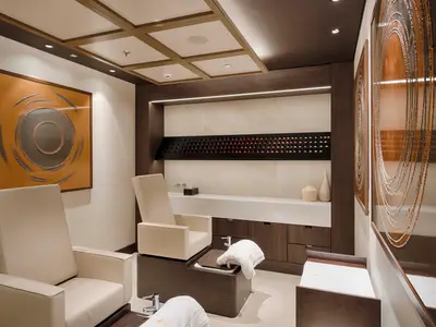 Luxuriöser Nagelpflegebereich an Bord der MSC World America. Zwei cremefarbene Sessel vor einer Theke mit Nagellack-Regalen. Modernes Design mit dunklem Holz, hellen Wänden und Kunstwerken.