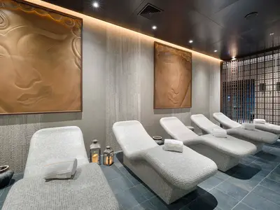 Ein stilvoller Entspannungsbereich im MSC Aurea Spa der MSC World America mit mehreren beigen Mosaik-Liegen. An den Wänden hängen zwei große Buddha-Reliefs, die eine ruhige Atmosphäre schaffen. Eine Gittertrennwand ist im Hintergrund sichtbar.