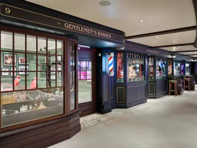 Ansicht des eleganten Gentlemen's Barber auf der MSC World America, gekennzeichnet mit einer klassischen Barbershop-Stange. Im Schaufenster sind Pflegeprodukte und rote Friseurstühle zu sehen.
