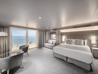 Eine geräumige und moderne Grand Suite Aurea an Bord der MSC World America. Das Schlafzimmer verfügt über ein Doppelbett, Sofa, Sitzbereich und einen Balkon mit Meerblick.